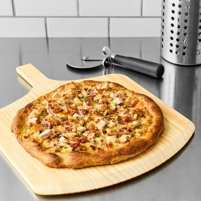 A delicious chicken and bacon pizza, featuring a creamy white sauce made with Cattlemen'S Alabama White Bbq Sauce, 0.5 Gal, is presented on a wooden pizza peel.