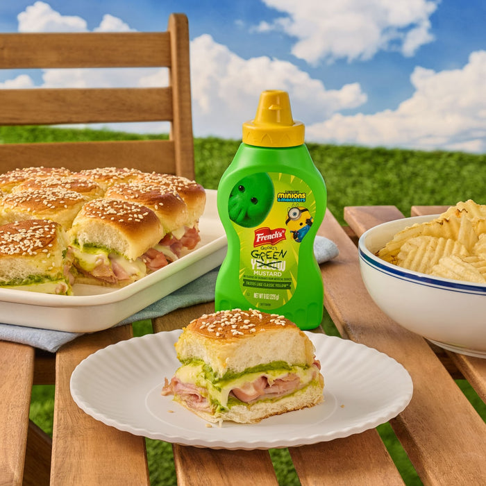 A bottle of French'S Goomi'S Green Mustard, 8.0 Oz, is displayed on a picnic table next to a plate of ham and cheese sliders made with the green mustard.