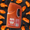 A gallon jug of Frank's RedHot Original Cayenne Pepper Sauce next to a plate of chicken wings.