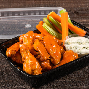 A close-up of a container of buffalo wings with celery sticks, carrots, and blue cheese dip.