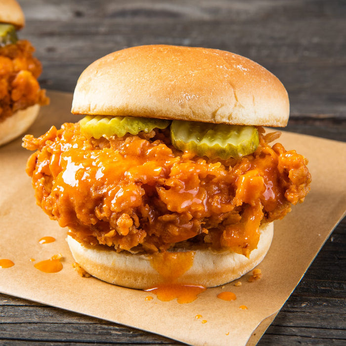 A close-up of a spicy fried chicken sandwich with pickles on a bun.