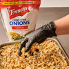 ["A hand in a black glove sprinkles French's Crispy Fried Onions on a casserole of green beans."]