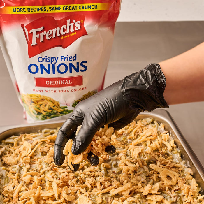 ["A hand in a black glove sprinkles French's Crispy Fried Onions on a casserole of green beans."]