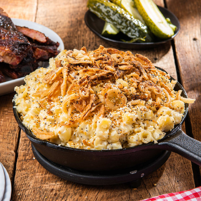 ['A close-up of a cast iron skillet filled with macaroni and cheese topped with crispy fried onions and sesame seeds.']