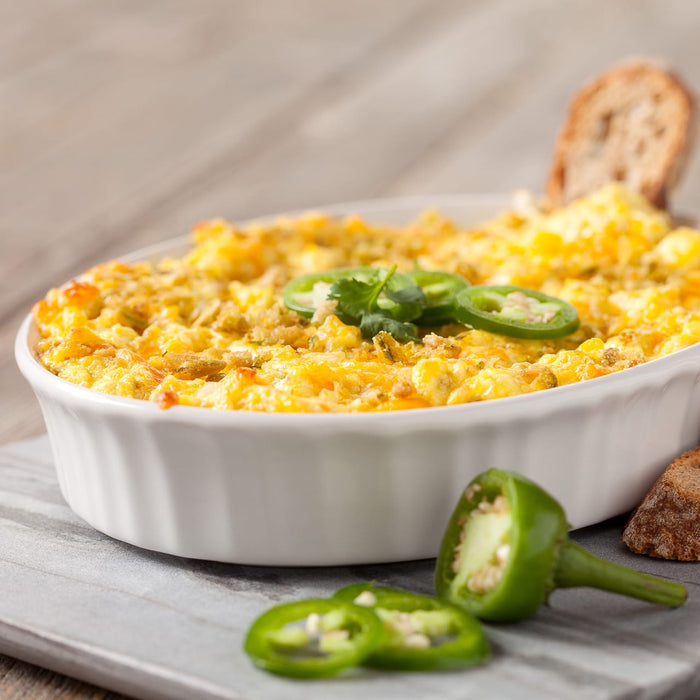 ['A white casserole dish filled with a cheesy dip topped with jalapenos and cilantro.']