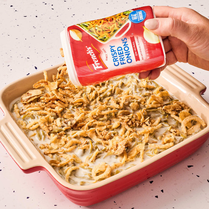 ["A hand sprinkles French's Crispy Fried Onions on a casserole dish of green beans."]