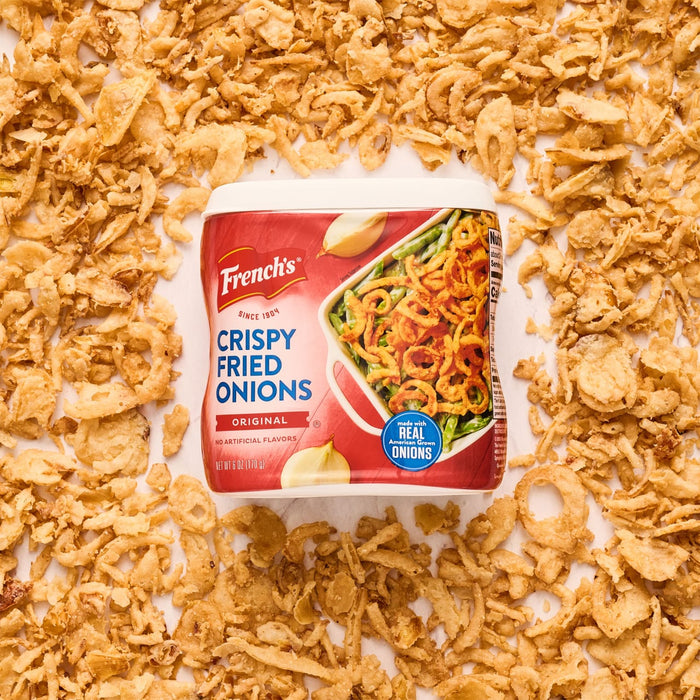 ["A box of French's Crispy Fried Onions with a pile of fried onions in the background."]