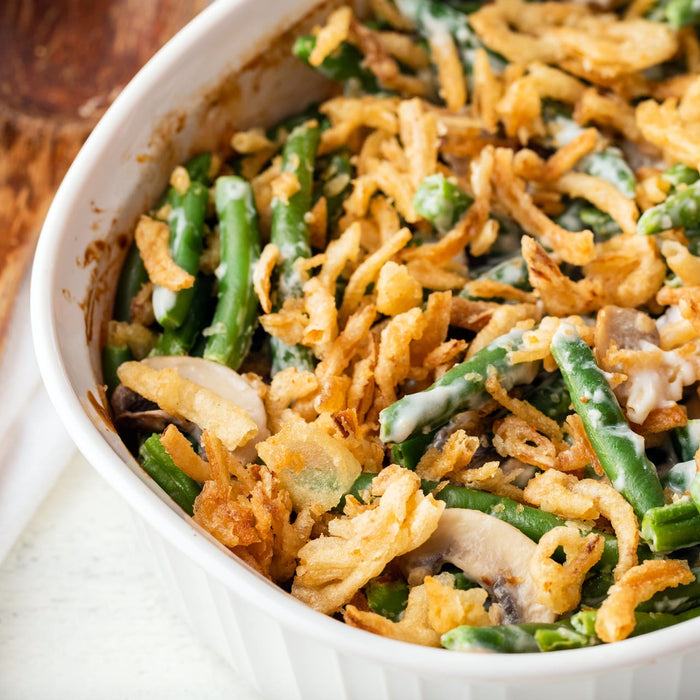['A white bowl filled with green bean casserole topped with crispy fried onions.']