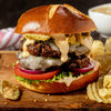 A double cheeseburger with fried pickles, lettuce, tomato, and onion on a pretzel bun.