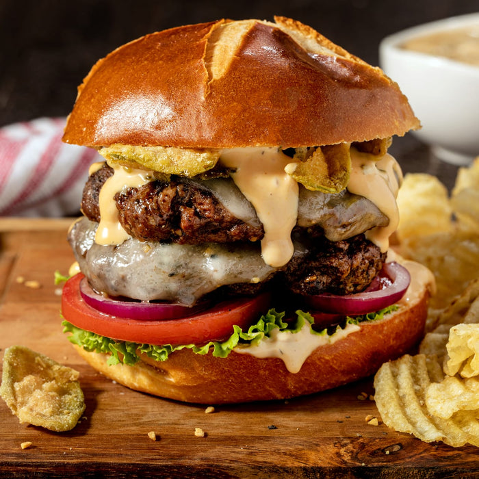 A double cheeseburger with fried pickles, lettuce, tomato, and onion on a pretzel bun.