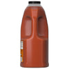 A side profile of a large, clear plastic jug of Franks Red Hot Original Buffalo Wing Hot Sauce Red Hot 128 Oz, showing its built-in handle and black screw-top cap.