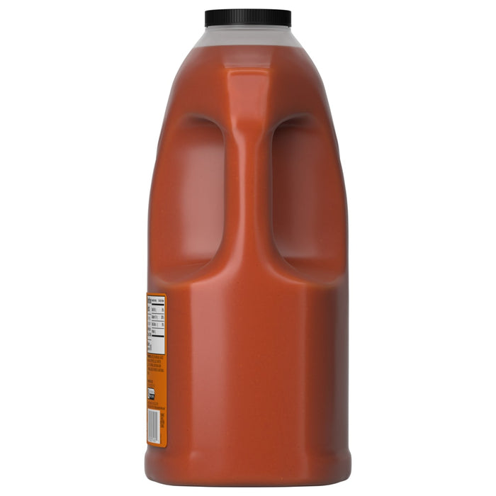 A side profile of a large, clear plastic jug of Franks Red Hot Original Buffalo Wing Hot Sauce Red Hot 128 Oz, showing its built-in handle and black screw-top cap.