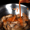 A bowl of chicken wings being drizzled with hot sauce.