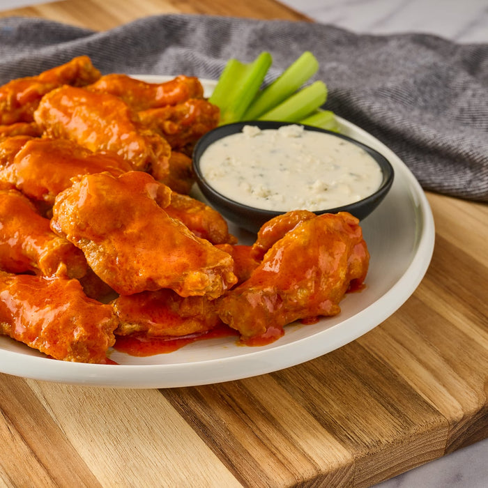 ['A plate of buffalo wings with celery sticks and blue cheese dip.']