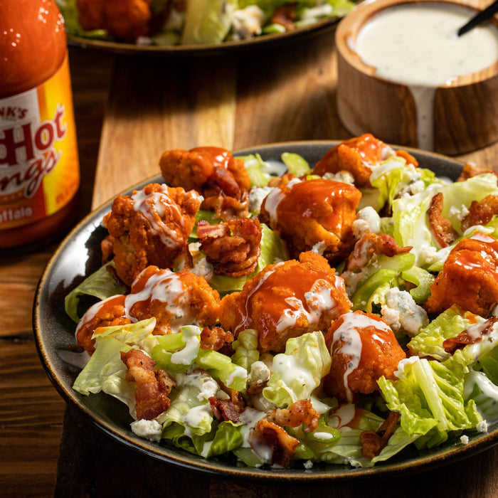 ['A plate of buffalo chicken salad with blue cheese, bacon, and ranch dressing.']
