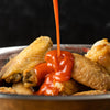 A close-up of chicken wings being drizzled with hot sauce.