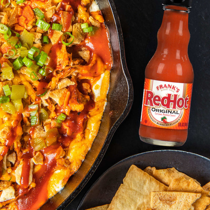 A bowl of buffalo chicken dip with pita chips and a bottle of Frank's RedHot Original Cayenne Pepper Sauce.