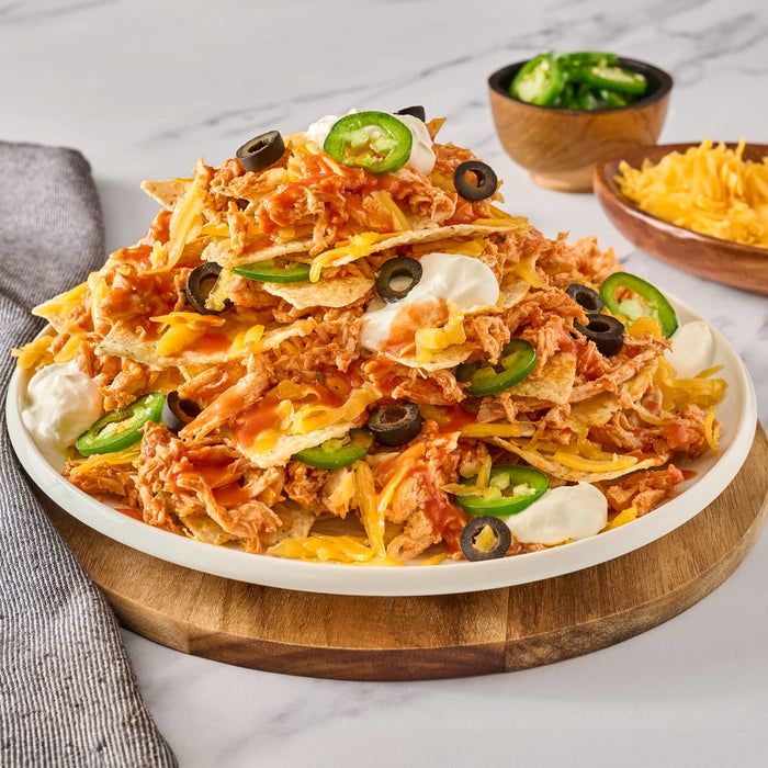 A plate of nachos with chicken, cheese, sour cream, jalapenos, and black olives.