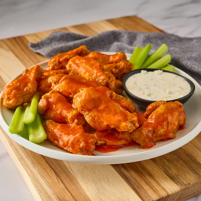 A plate of buffalo wings with celery sticks and blue cheese dressing.
