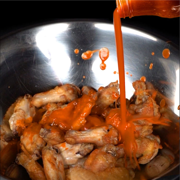 ['A bowl of chicken wings being drizzled with hot sauce.']