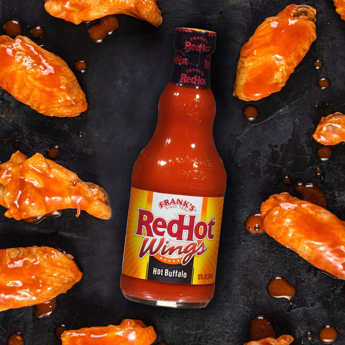 ["A bottle of Frank's RedHot sauce with a label that says 'RedHot Wings' and 'Hot Buffalo' is surrounded by chicken wings"]