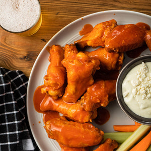 ['A plate of buffalo wings with blue cheese dressing and celery sticks.']
