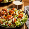 ['A plate of buffalo chicken salad with blue cheese, bacon, and ranch dressing.']