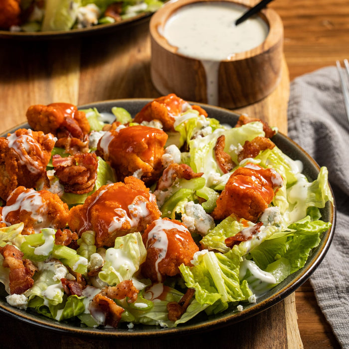 ['A plate of buffalo chicken salad with blue cheese, bacon, and ranch dressing.']