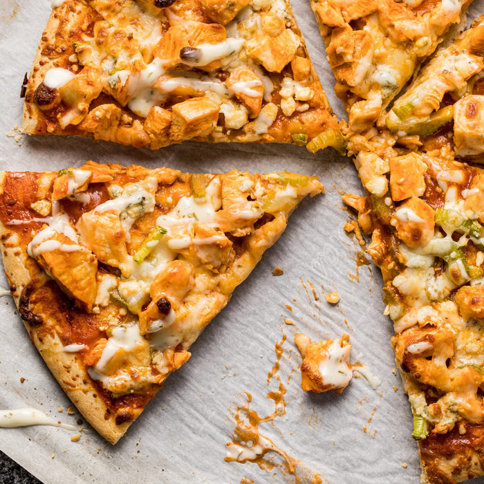 ['A close-up of three slices of buffalo chicken pizza with ranch dressing on parchment paper.']