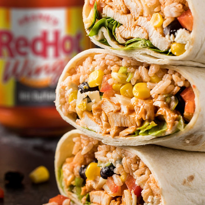 ['A stack of three RedHot Buffalo Chicken Burritos with corn, black beans, rice, and lettuce.']