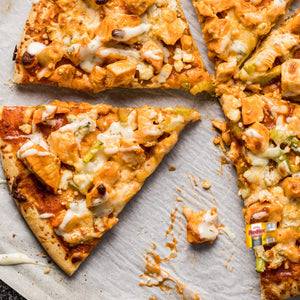 A man in a white hat and gloves cuts a pizza with a pizza cutter in a kitchen.