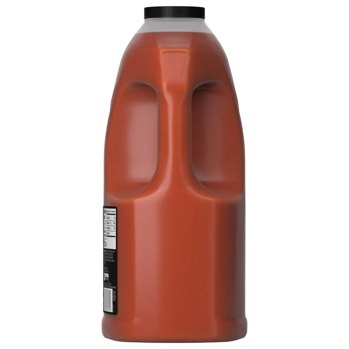 A side view of a large, 128-ounce jug of Franks Red Hot Buffalo Wing Hot Sauce Extra Hot 128 Oz, showing the built-in handle and the reddish-orange sauce inside.
