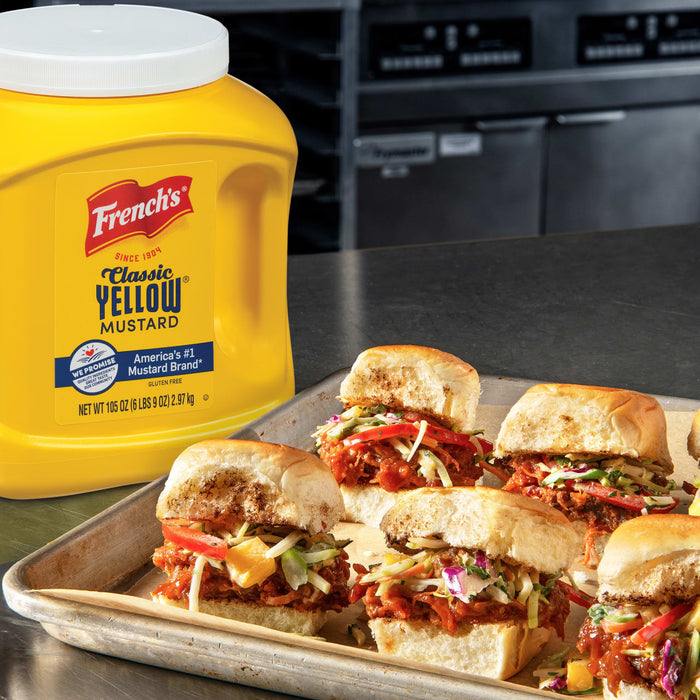 A container of Frenchs Classic Yellow Mustard next to a tray of pulled pork sliders.