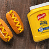A jar of Frenchs Classic Yellow Mustard next to two hot dogs with mustard.