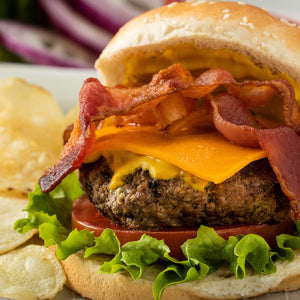 A close-up of a cheeseburger with bacon, lettuce, and tomato on a sesame seed bun.