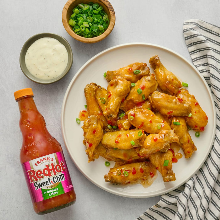 A plate of Frank's RedHot Sweet Chili chicken wings is displayed with dipping sauce and chopped green onions.
