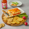 A block of cream cheese topped with Frank's RedHot Sweet Chili sauce is served with crackers, celery, and radishes.
