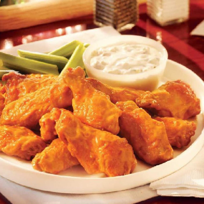 A plate of buffalo wings with celery sticks and a bowl of blue cheese dressing.