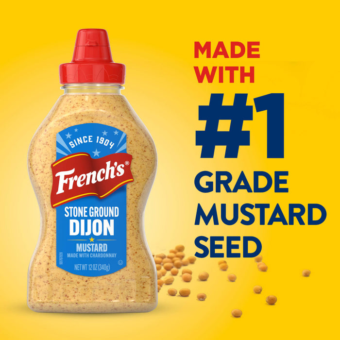 A bottle of Frenchs Beige Stone Ground Dijon Mustard 12 Oz is displayed against a bright yellow background with scattered mustard seeds and text highlighting that it is made with number one grade mustard seed.