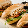 A row of grilled chicken sandwiches on crusty rolls featuring fresh arugula, sliced tomatoes, and a creamy spread made with Frenchs Beige Stone Ground Dijon Mustard 12 Oz.