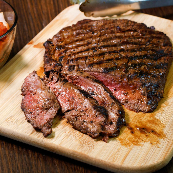 A perfectly grilled flank steak rests on a wooden cutting board alongside a bowl of Frenchs Beige Stone Ground Dijon Mustard 12 Oz for a flavorful meal.