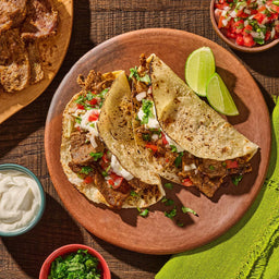 Three street tacos filled with steak and fresh toppings are seasoned with Cholula Medium Chili Garlic Taco Seasoning Mix 1 Oz and served on a clay plate with lime wedges.