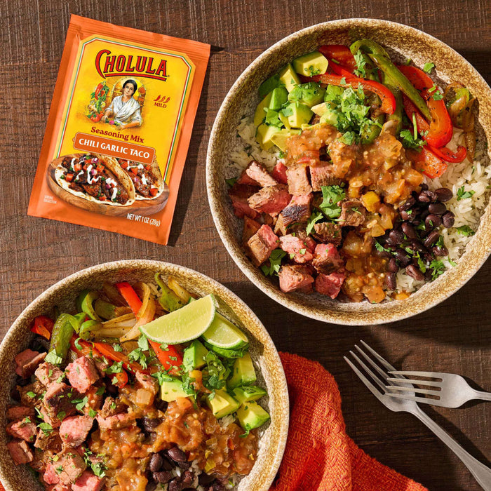 Two steak burrito bowls topped with avocado and salsa are served alongside a packet of Cholula Seasoning Mix Chili Garlic Taco.