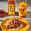 A yellow plate with a taco topped with red cabbage, cilantro, and a creamy sauce, next to a glass of mango margarita with a chili lime seasoning rim, and a bottle of Cholula Chili Lime seasoning.