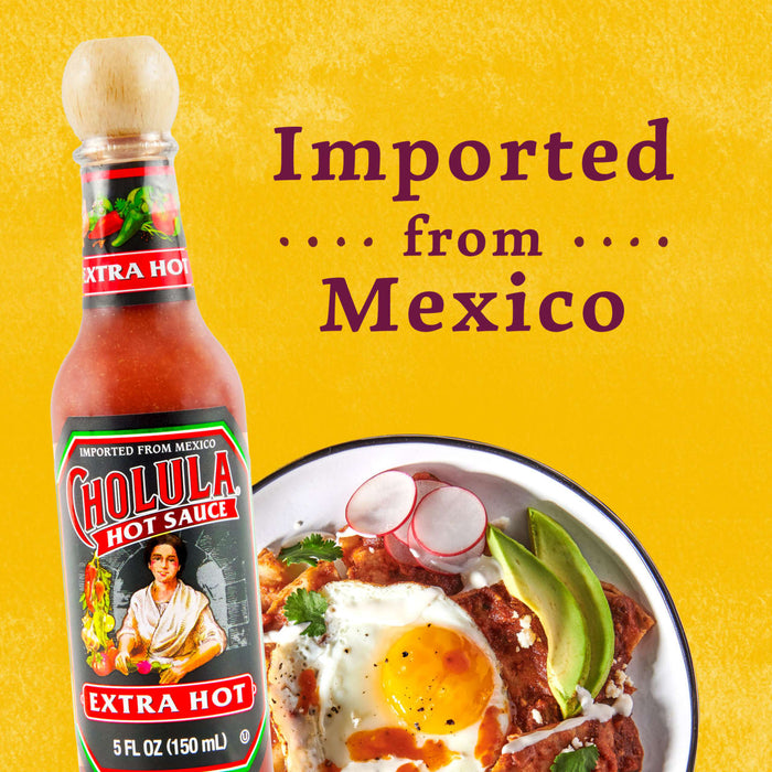 A bottle of Cholula Hot Sauce, Extra Hot, with a bowl of Mexican food in the background.