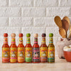 Eight bottles of Cholula hot sauce in different flavors are lined up on a counter.