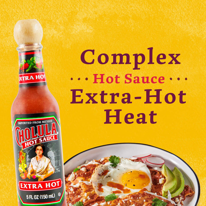 A bottle of Cholula Extra Hot Hot Sauce next to a plate of Mexican food with a fried egg, avocado, and radish.