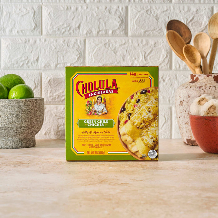 A box of Cholula Chicken Tinga Taco Kit is displayed on a counter with limes and kitchen utensils.