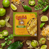 A Cholula brand frozen quesadilla meal is displayed amidst fresh ingredients like limes, jalapeA?os, and cilantro, suggesting a flavorful and spicy culinary experience.