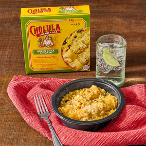 A Cholula brand frozen meal is displayed with a serving in a bowl, a fork, and a glass of water with lime on a red cloth.